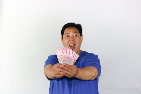 Portrait of a happy Indonesian male celebrating financial success while holding money
