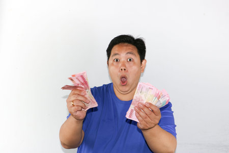 Portrait of a happy Indonesian male celebrating financial success while holding money