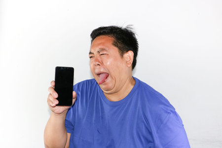 Portrait of Indonesian guy crying and holding smartphone, expressing deep sadness and disappointment