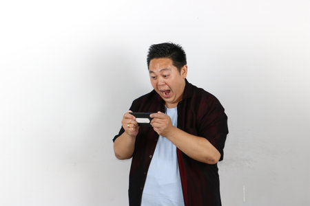 Portrait of cheerful Indonesian male holding up a mobile phone while gesturing toward the empty displayの写真素材