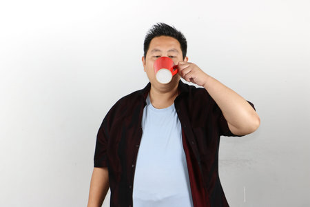 Portrait of Asian man drinking from a red mug against a isolated white background in studioの写真素材