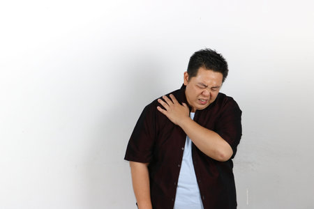 Indonesian guy suffering from shoulder pain and muscle injuries