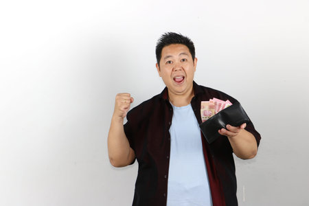 Portrait of Happy Asian man holding an open black wallet full of Indonesian Rupiah money