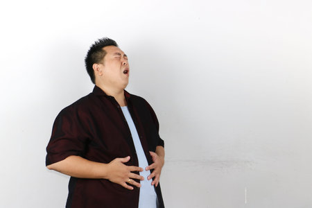 An Indonesian man holding his stomach tightly suffering from very bad stomach ache, diarrheaの写真素材
