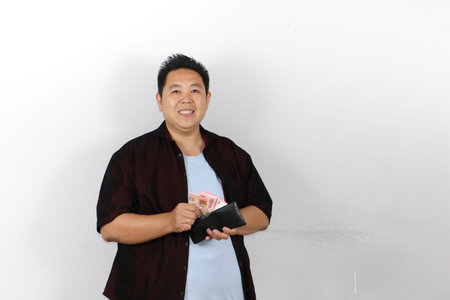 Portrait of Happy Asian man holding an open black wallet full of Indonesian Rupiah moneyの写真素材