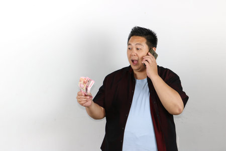 Shocked expression and happy gesture of Asian man holding money and smartphoneの写真素材