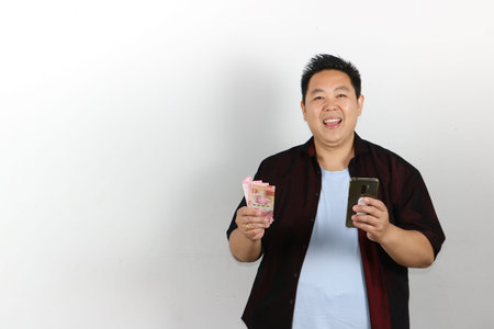Shocked expression and happy gesture of Asian man holding money and smartphone