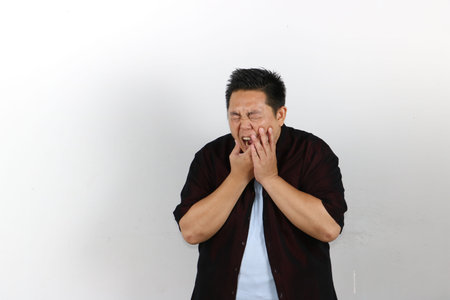 Indonesian Asian Man puts his hand on his mouth and feels toothache because of tooth decay.の写真素材
