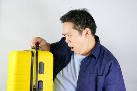 Portrait of an asian man ready for vacation carrying a vibrant yellow travel luggage