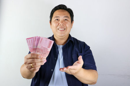 Portrait of a joyful Indonesian man holding cash money on isolated white background