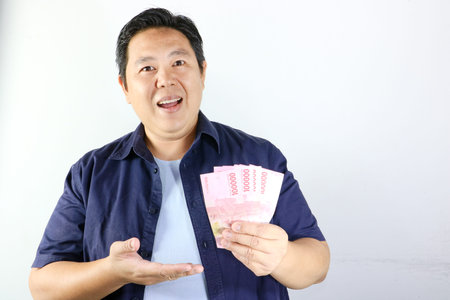 Happy Asian man holding Indonesian Rupiah banknotes and smiling on white background