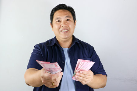 Smiling mature male holding rupiah cash signifying financial freedom and prosperity in Indonesia
