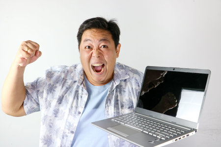 Angry Asian man shouting in frustration while holding a laptop computer