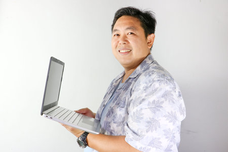 Portrait of Indonesian man looking happy and confident while holding a modern laptop
