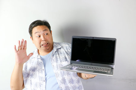 Surprised Asian man with saying no gesture holding silver laptop