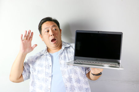 Surprised Asian man with saying no gesture holding silver laptop