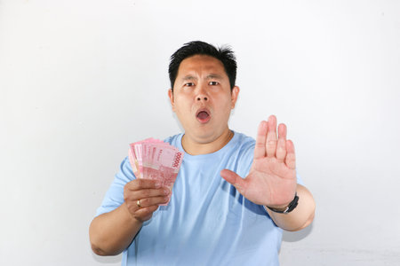 Portrait of Asian man shows saying NO expression while holding Indonesian Rupiah banknotes