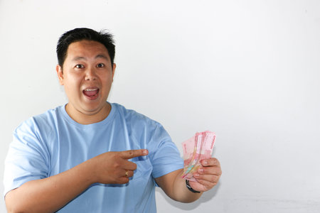 Happy Asian man showing a huge smile while holding a lot of Indonesian Rupiah banknotes in both...