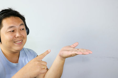 Happy Asian man enjoying music with wireless headphones and pointing his finger to the side.の写真素材