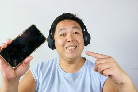 Cheerful asian man with mouth open in surprise watching exciting media content on a mobile phoneの写真素材