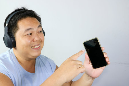 Cheerful asian man with mouth open in surprise watching exciting media content on a mobile phoneの写真素材