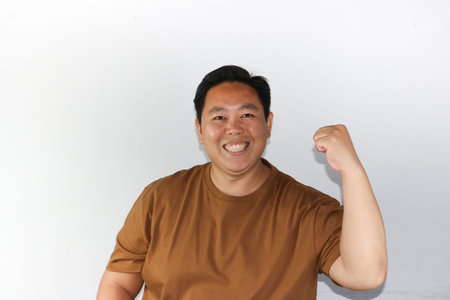 Enthusiastic Asian man celebrating success with a winning gesture and bright smile in studio settingの写真素材