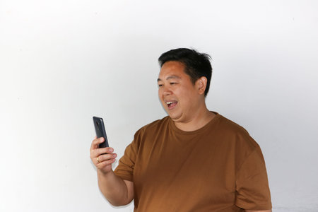 Smiling Asian man holding a smartphone with a blank screen towards the camera for app mockupsの写真素材