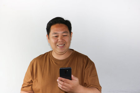 Smiling Asian man holding a smartphone with a blank screen towards the camera for app mockupsの写真素材