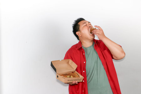 Asian man in red shirt enjoying a delicious piece of martabak manis from a cardboard snack boxの写真素材