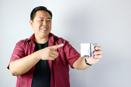 Adult Asian man smiling and presenting a small stainless steel gift box on isolated white backgroundの写真素材