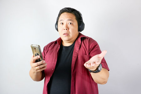 Portrait of Pensive Asian man wearing headphones looking at his smartphone screenの写真素材