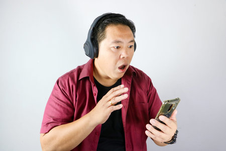 Portrait of Pensive Asian man wearing headphones looking at his smartphone screenの写真素材