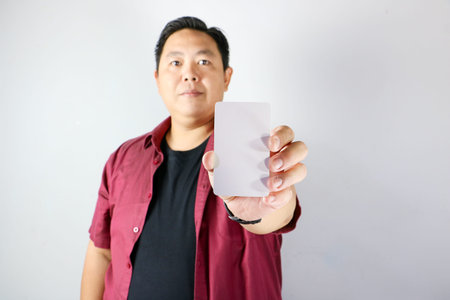 Asian man smiling while holding blank white business card for mock up presentationの写真素材