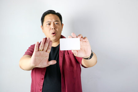 Asian man showing stop gesture with palm facing forward for refusal or no access while holding white paperの写真素材