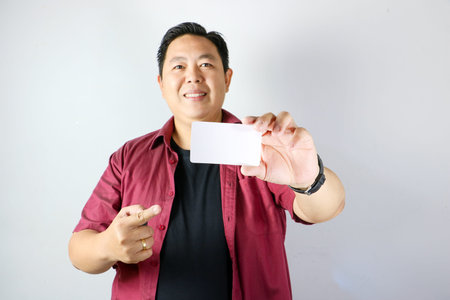 Asian man smiling while holding blank white business card for mock up presentationの写真素材