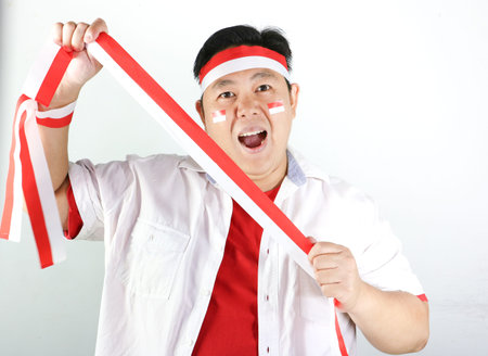 Portrait of a happy Indonesian man showing red and white ribbon for Independence Day, isolated on white background.の写真素材