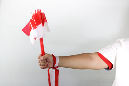 Hand holding three small Indonesian flags with red and white ribbon decoration on white backgroundの写真素材