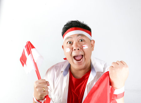 Enthusiastic Indonesian man holding small national flag and showing winning gesture on white backgroundの写真素材