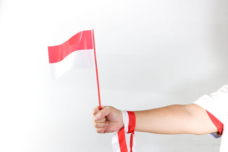 Hand holding three small Indonesian flags with red and white ribbon decoration on white backgroundの写真素材
