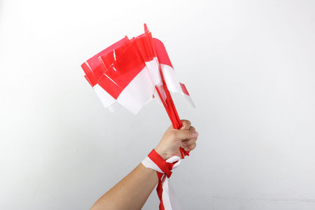 Hand holding three small Indonesian flags with red and white ribbon decoration on white backgroundの写真素材