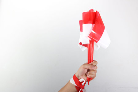 Hand holding three small Indonesian flags with red and white ribbon decoration on white backgroundの写真素材