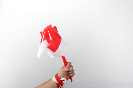 Hand holding three small Indonesian flags with red and white ribbon decoration on white backgroundの写真素材