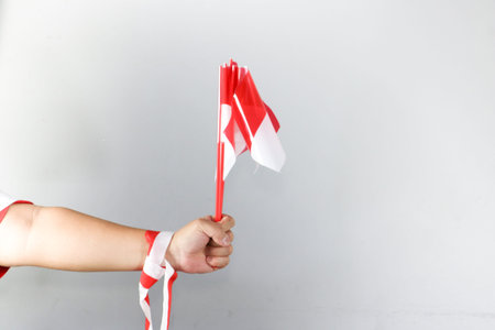 Hand holding three small Indonesian flags with red and white ribbon decoration on white backgroundの写真素材
