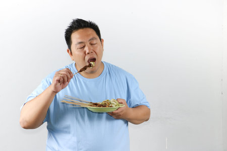 Portrait of Indonesian man eating delicious chicken satay with peanut sauce and lontong rice cakesの写真素材