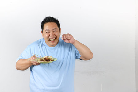 Portrait of Indonesian man eating delicious chicken satay with peanut sauce and lontong rice cakesの写真素材