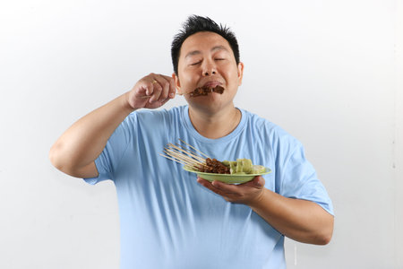 Portrait of Indonesian man eating delicious chicken satay with peanut sauce and lontong rice cakesの写真素材