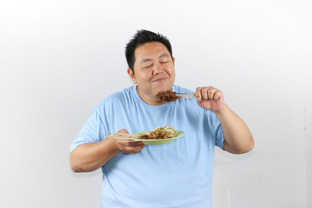 Portrait of Indonesian man eating delicious chicken satay with peanut sauce and lontong rice cakesの写真素材