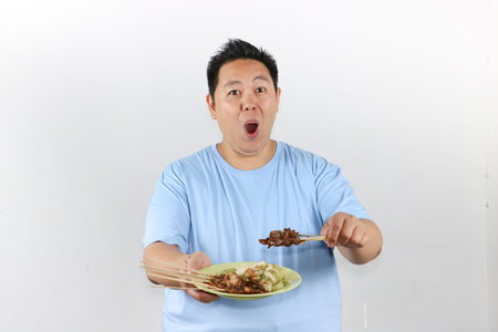 Happy Asian man holding a plate of authentic Indonesian chicken satay with peanut sauce and lontong rice cakesの写真素材