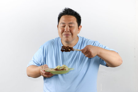 Happy Asian man holding a plate of authentic Indonesian chicken satay with peanut sauce and lontong rice cakesの写真素材