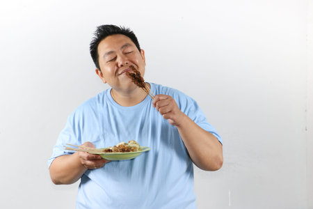 Portrait of an Asian man enjoying delicious grilled chicken skewers or sate ayam, isolated on white background.の写真素材